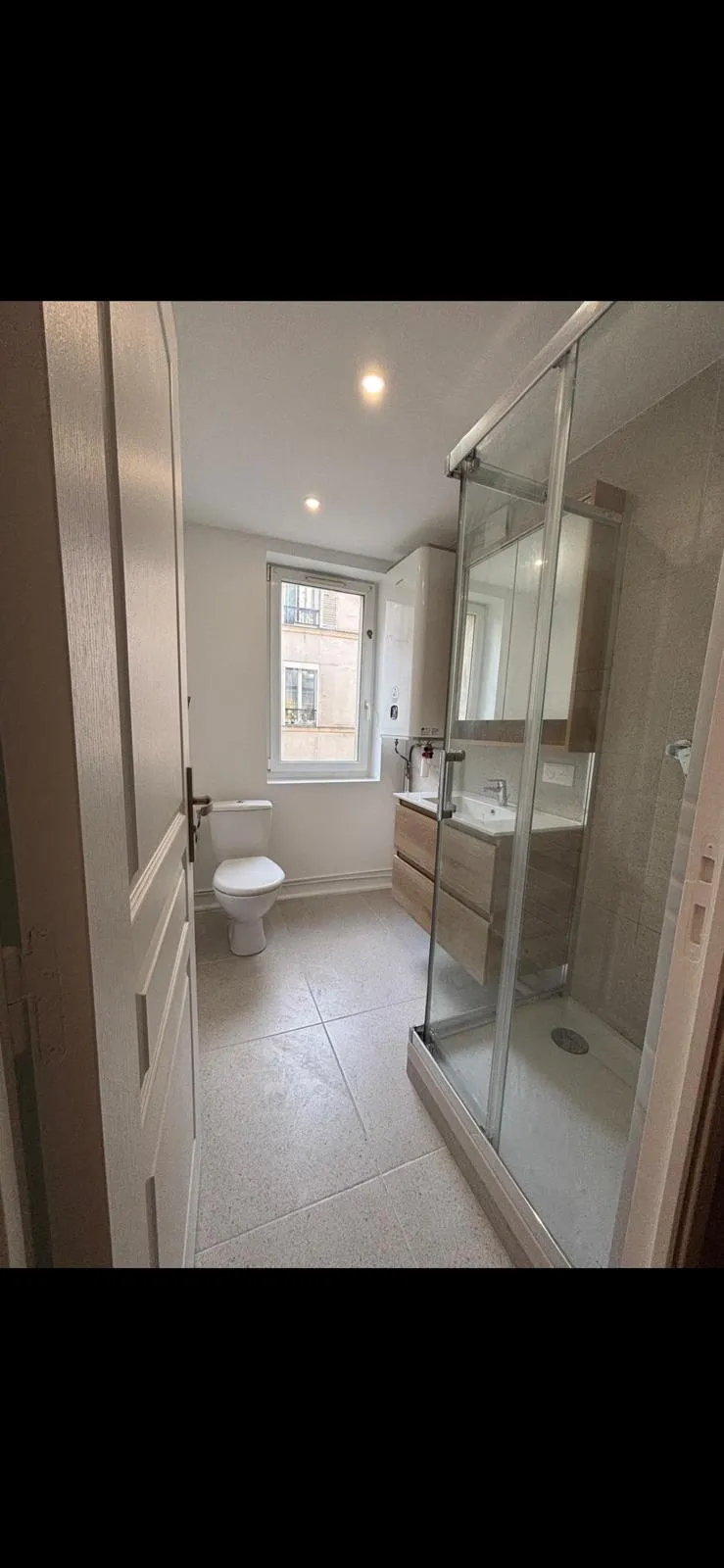 Salle de bain neuve du même appartement parisien : douche à l'italienne, paroi vitrée, meuble vasque et carrelage clair