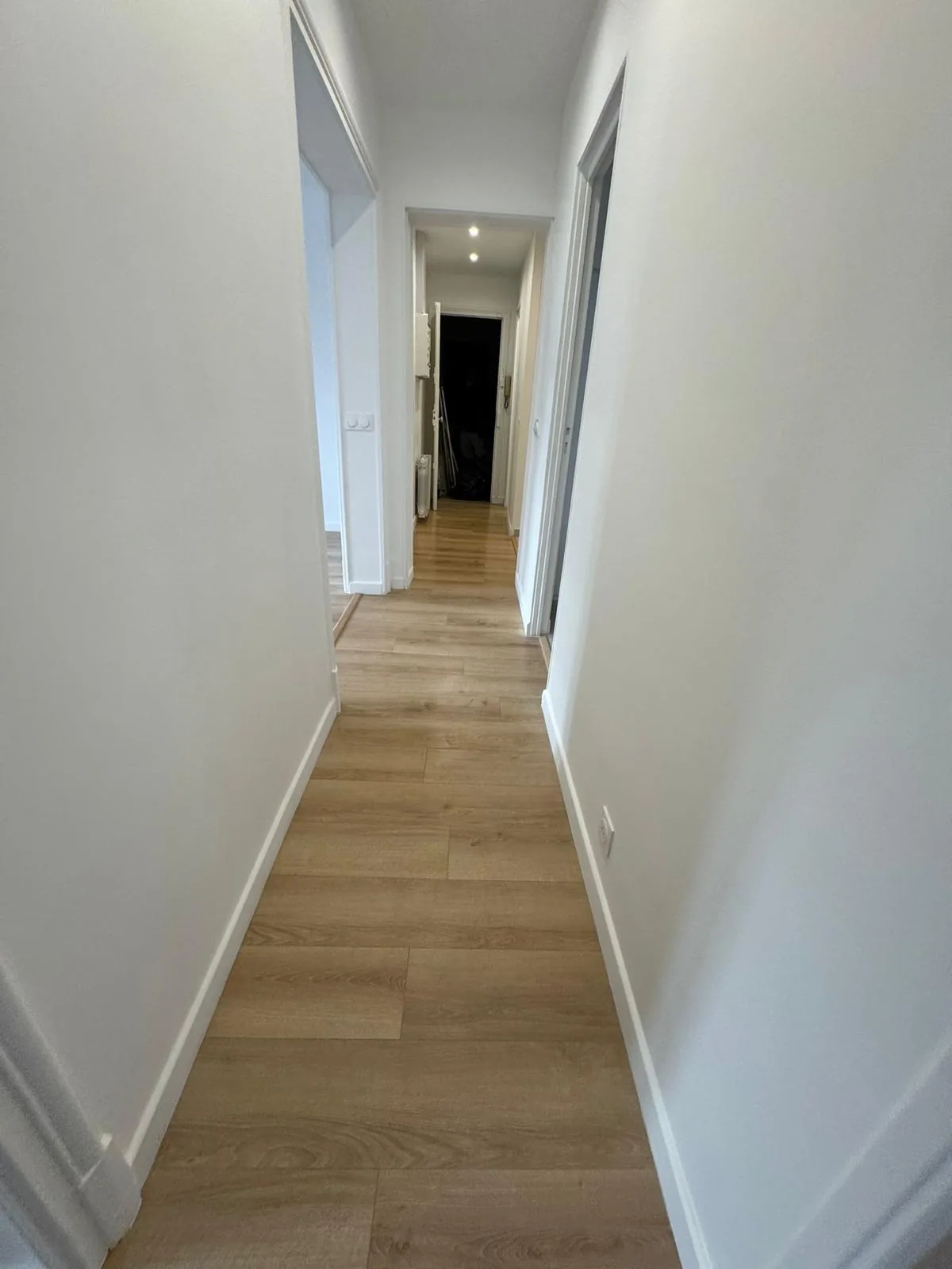 Le même couloir après rénovation par CK Bâtiment : parquet clair, murs blancs et plinthes neuves