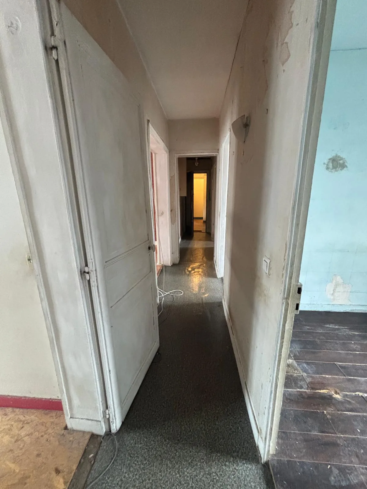 Couloir d'un appartement à Saint-Denis avant rénovation : murs écaillés, sol usé et menuiseries d'origine